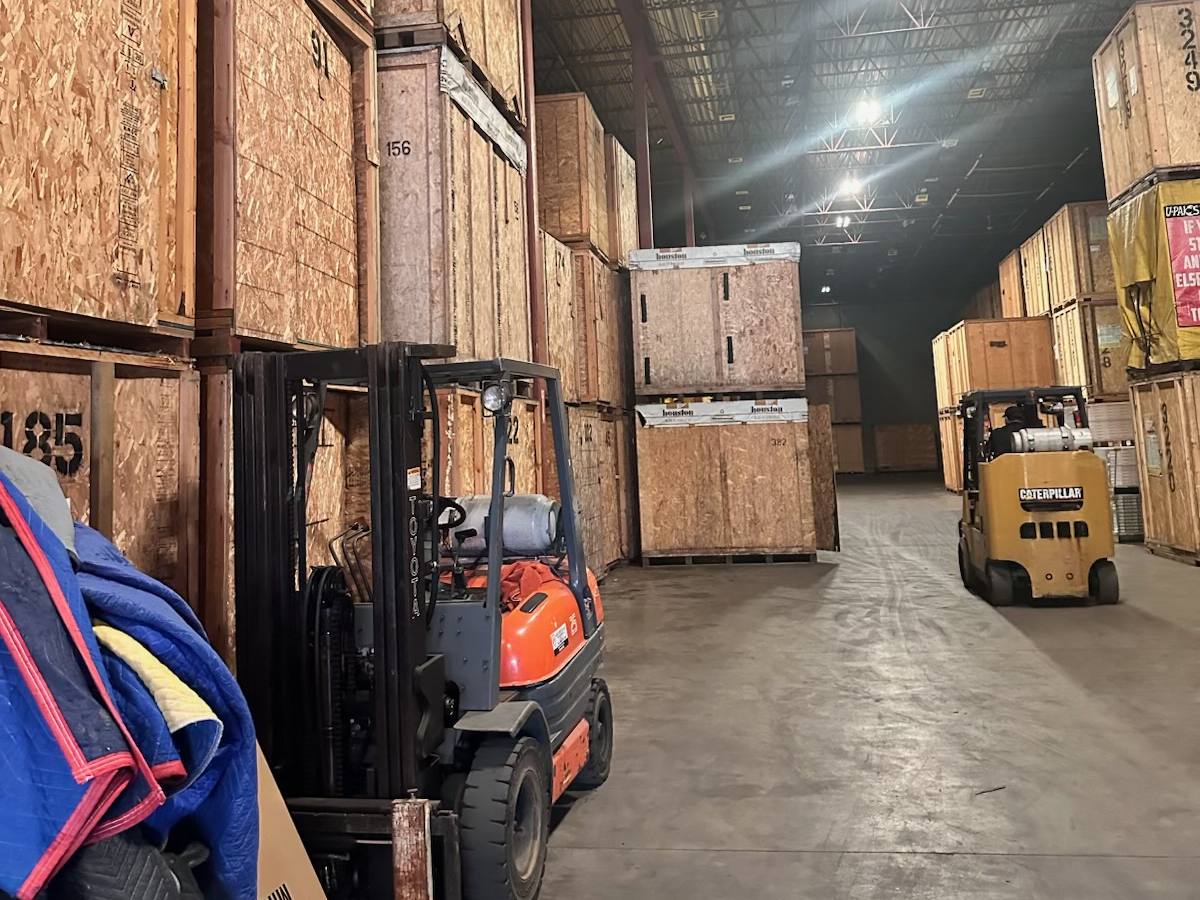 A warehouse aisle lined with numbered wooden storage vaults, with forklifts and moving blankets, photographed on one of our jobs in June 2026