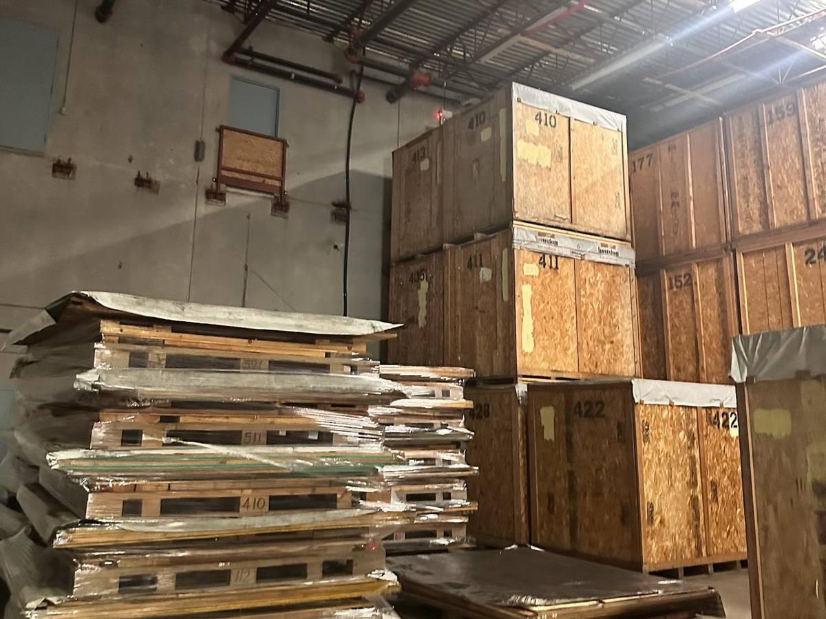 Numbered wooden storage vaults and pallets of wrapped panels in a warehouse, photographed on one of our jobs in June 2026