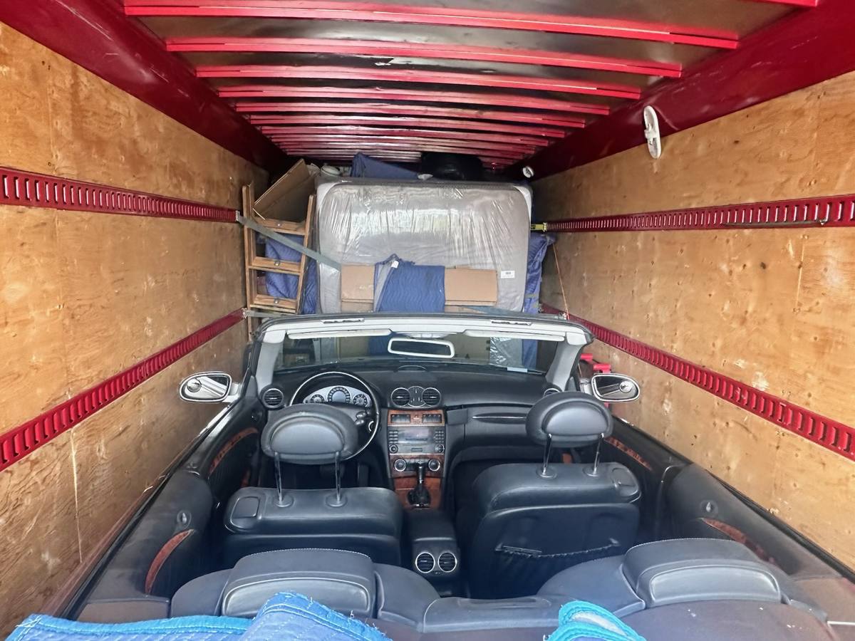 A convertible loaded on the floor of our moving truck with wrapped furniture strapped behind it, Calgary, May 2026