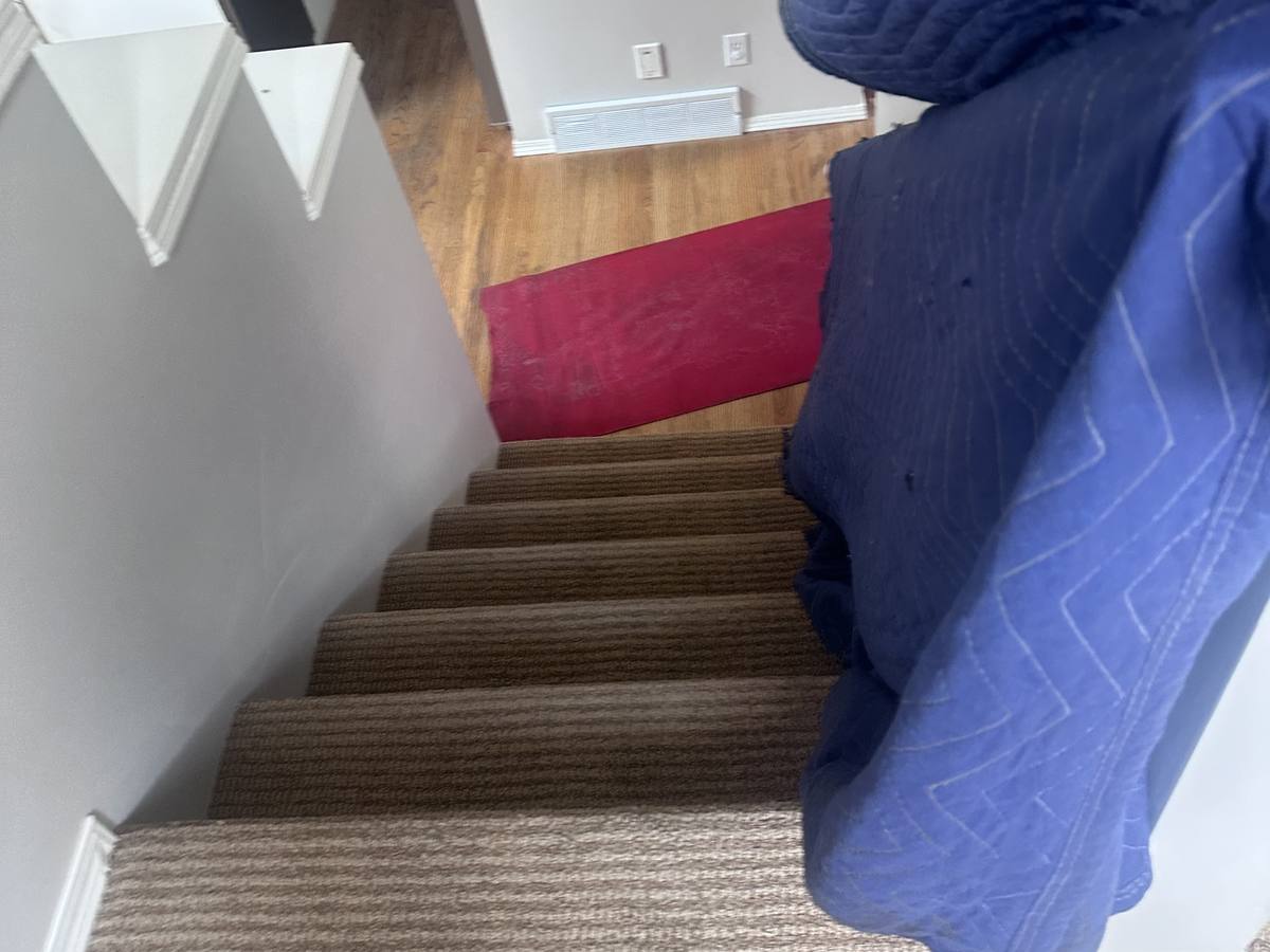 A blanket-wrapped piece of furniture on its way down a carpeted staircase during one of our Calgary moves, June 2025