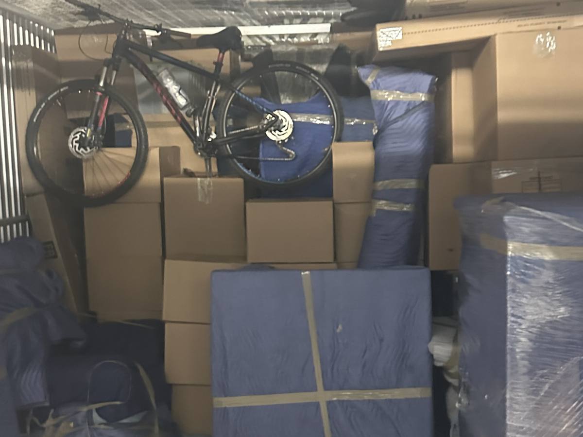 A storage unit packed with boxes, blanket-wrapped furniture and a bicycle on one of our Calgary storage jobs, May 2024
